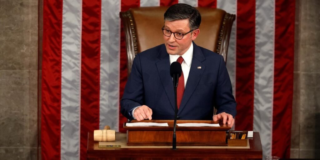 House Speaker Mike Johnson stands at a podium in the U.S. Capitol, addressing a tense crowd of lawmakers with a gavel in hand, as Republican and Democratic members react to a contentious spending bill debate amid a looming government shutdown threat.