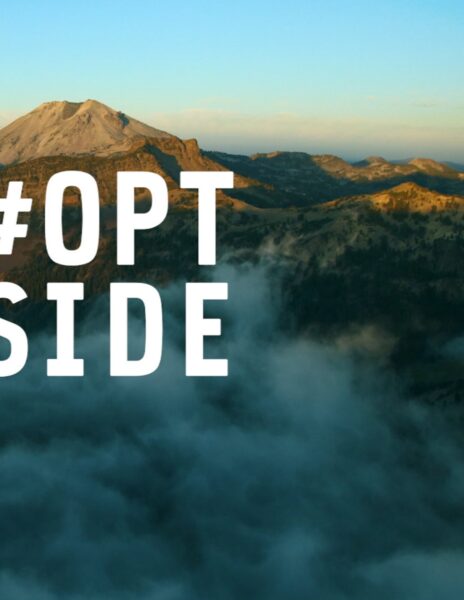 Aerial mountain landscape above clouds with bold white #OPTOUTSIDE hashtag text overlay.